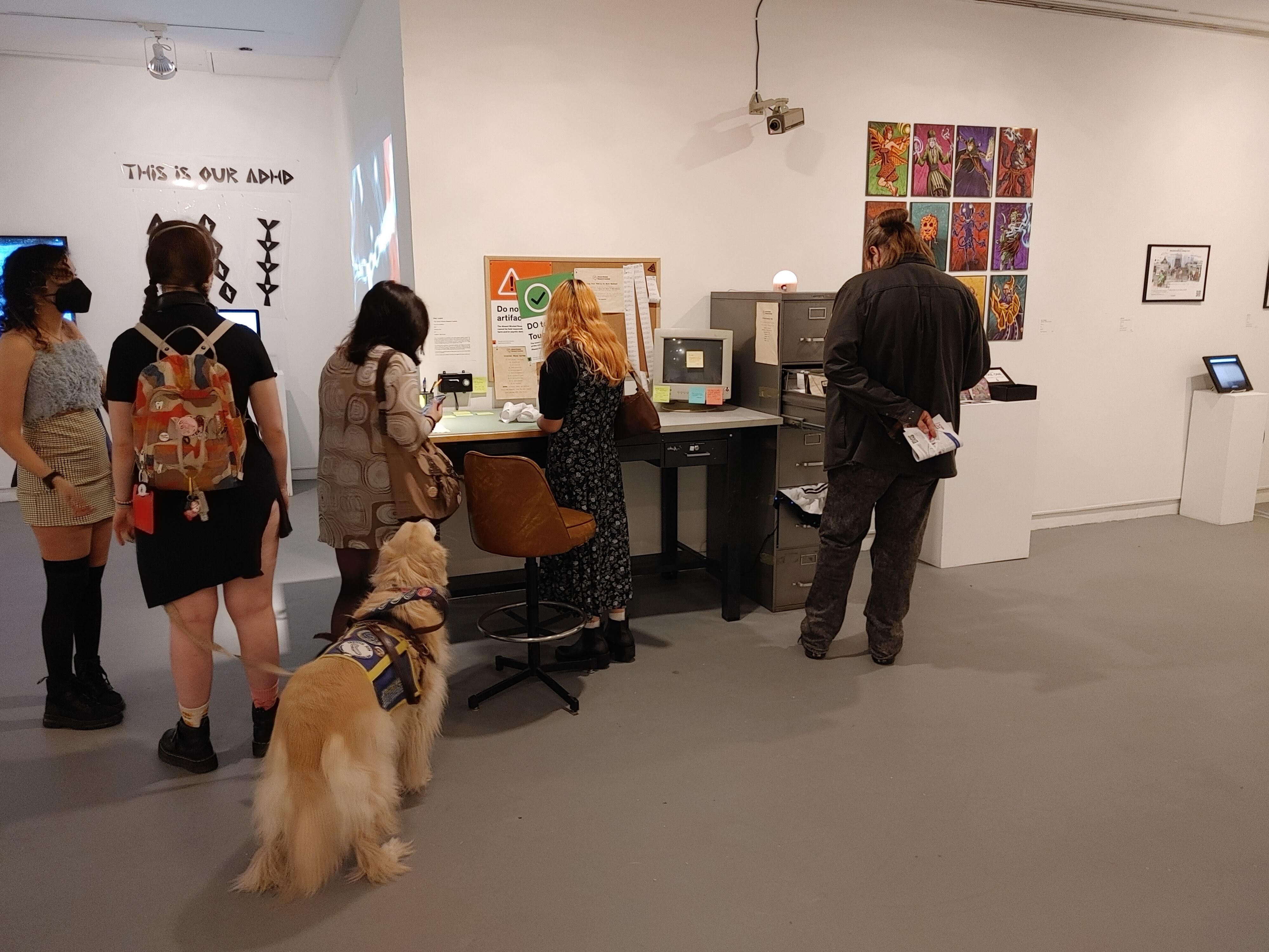 Photograph of thesis project on display. Several people and a dog are standing in front of it.