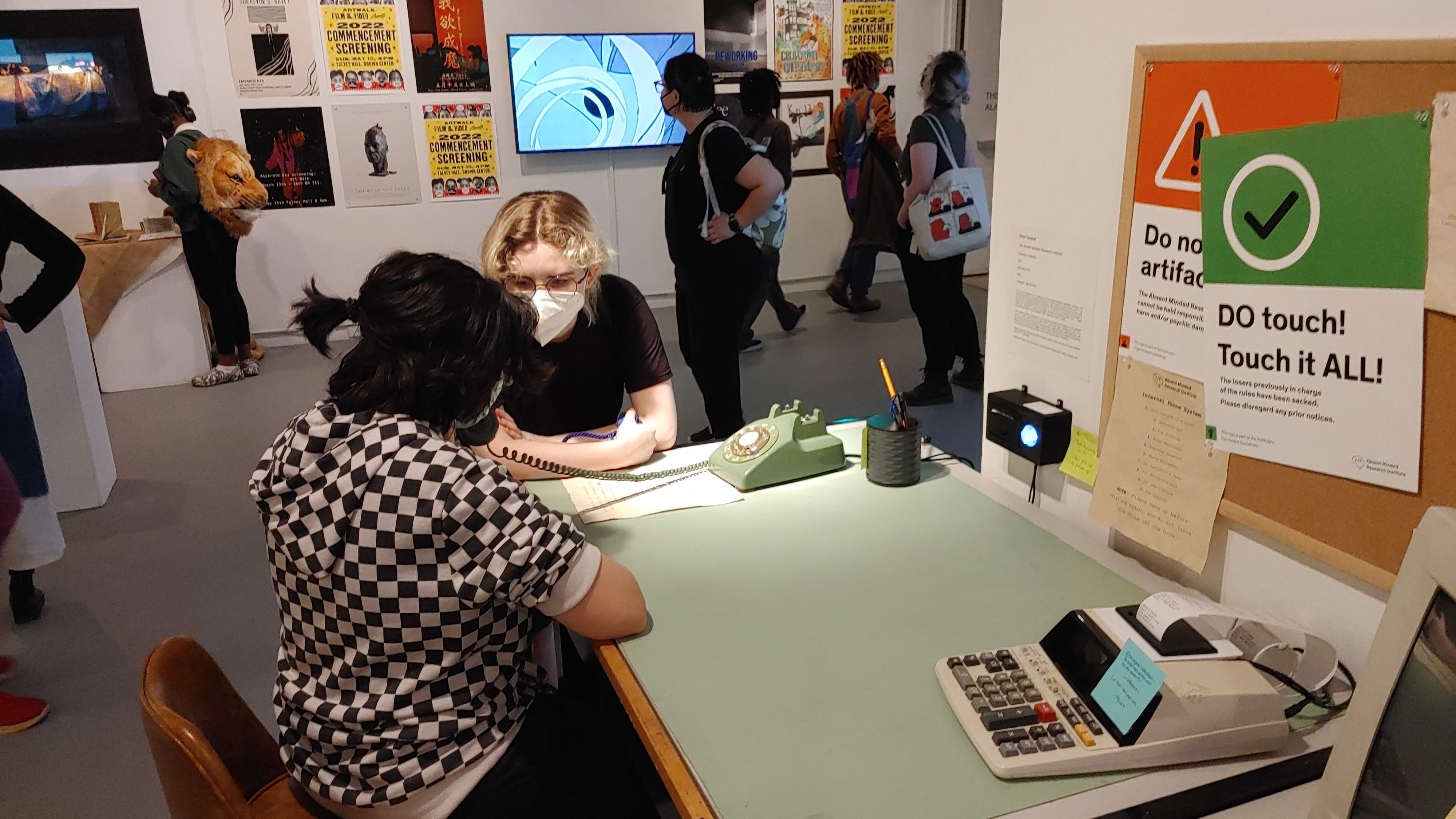 Photograph of thesis project on display. Two people are listening to the rotary phone on the desk.